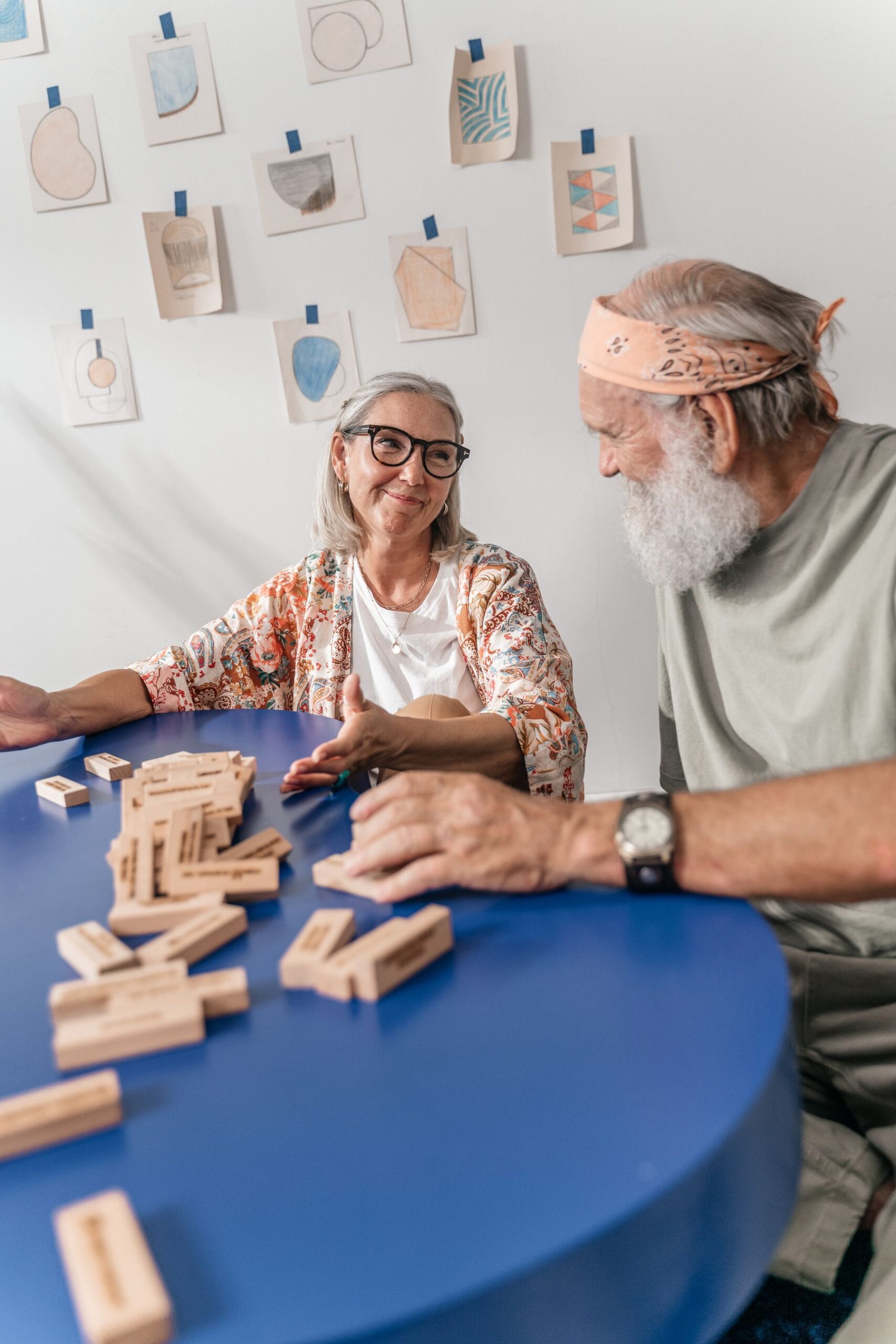 A senior couple smiling while playing a wooden block game at a blue table