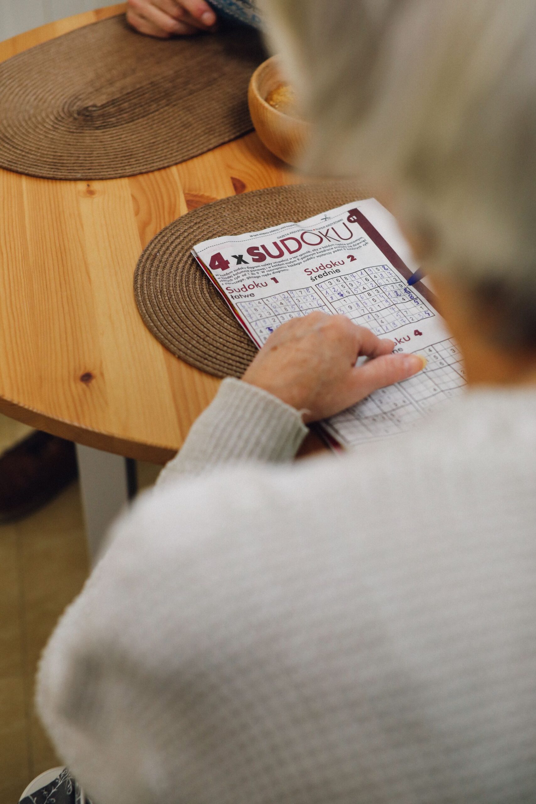 Close-up of an older adult solving a sudoku puzzle at a wooden table