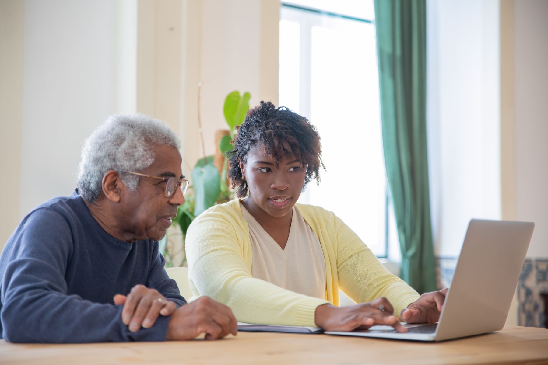 A care professional sitting beside an older man and guiding him through a laptop screen