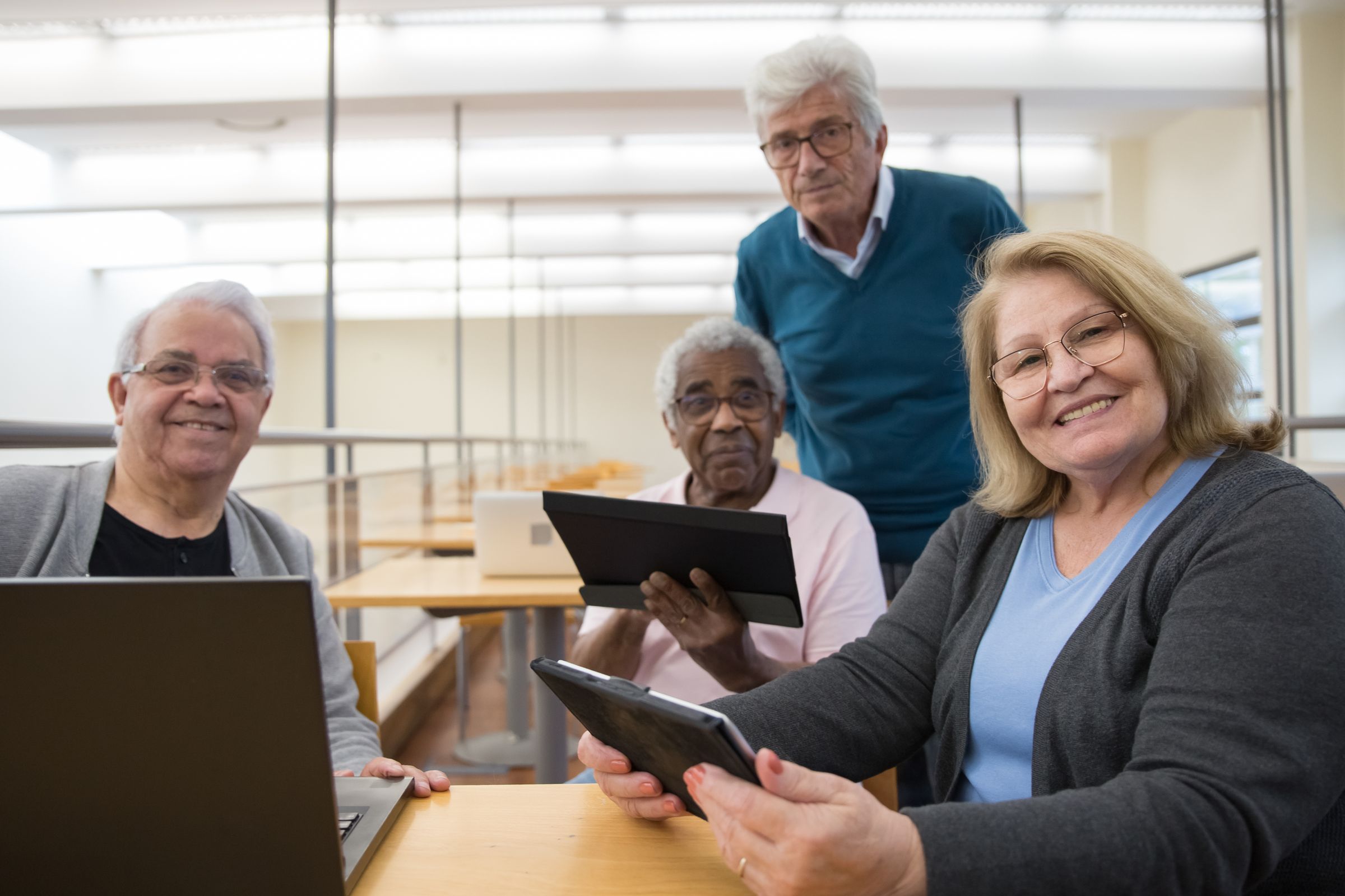 Group of older adults using tablets and laptops together in a bright training room
