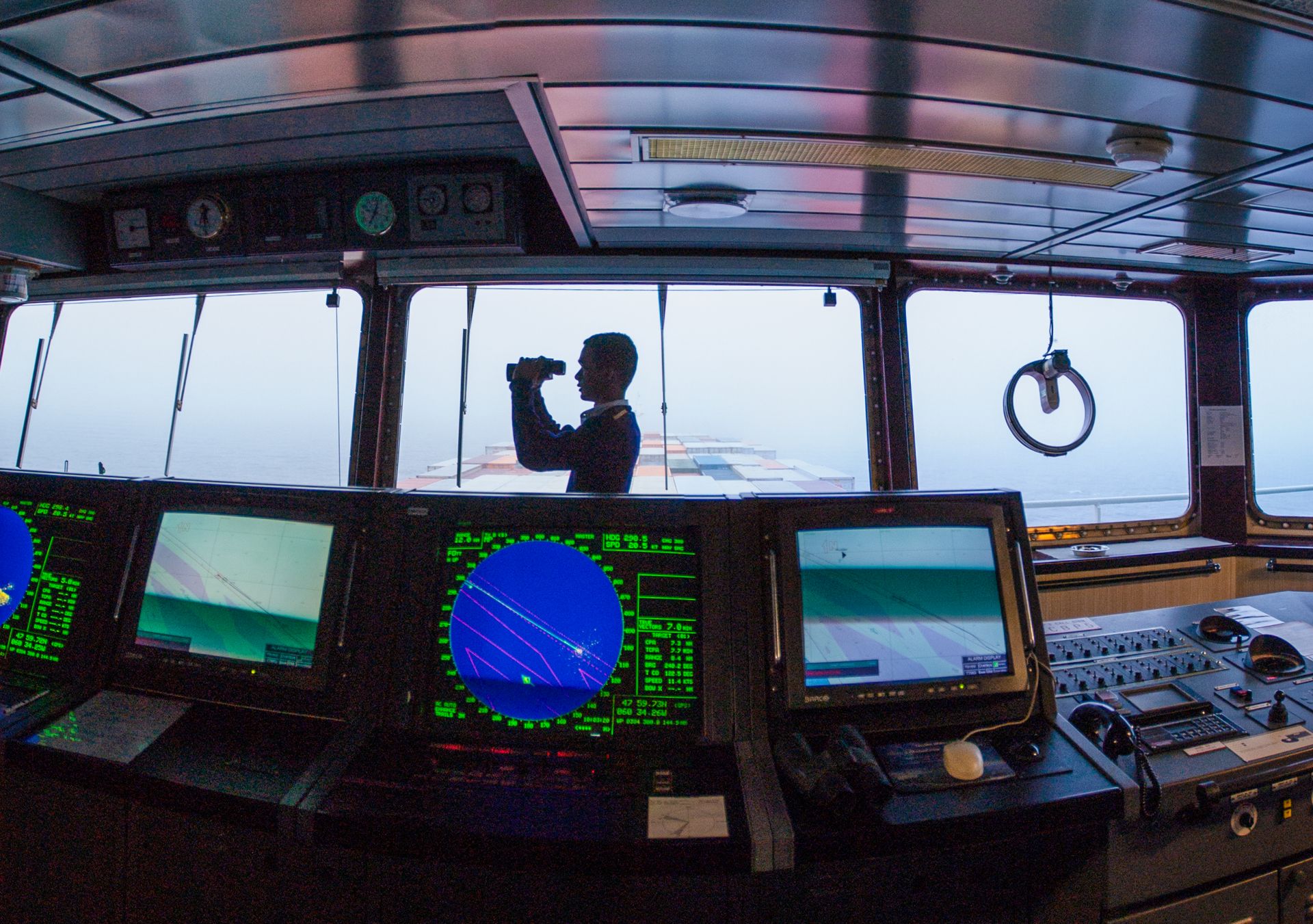 Navigator on a cargo ship bridge using binoculars