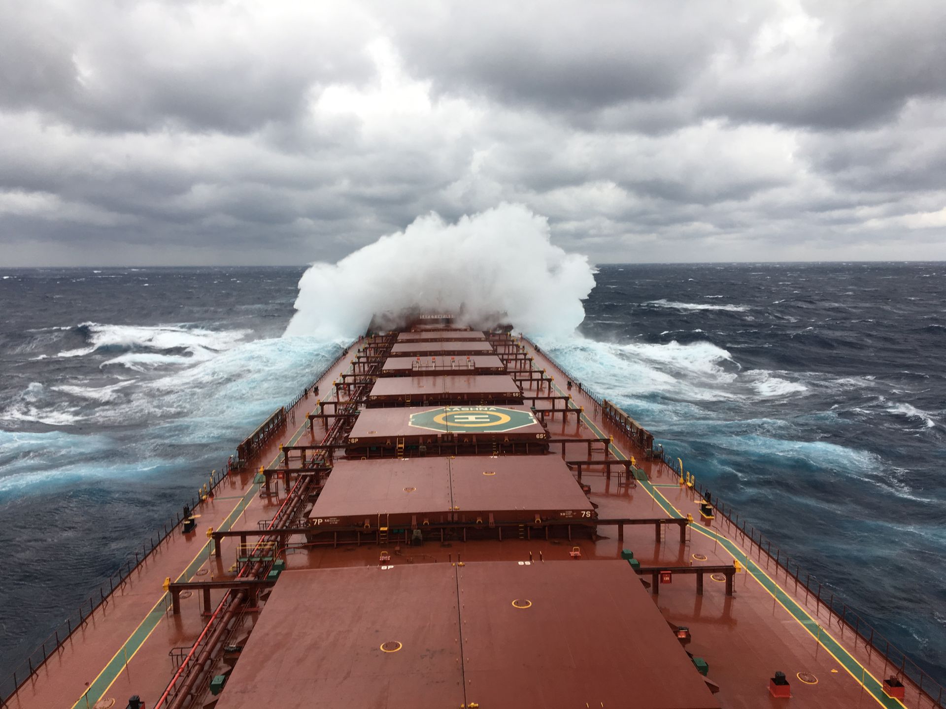 Cargo ship braving rough seas with waves crashing over the deck